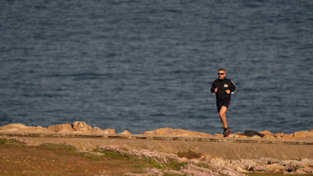 A man runs along a rocky shore with ocean in the background, showcasing fitness and tranquility.